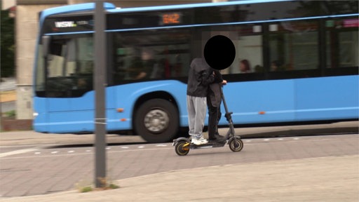Zwei Fahrer auf einem E-Scooter dahinter ein fahrender Bus