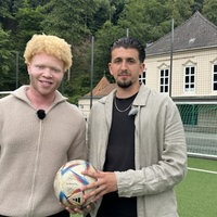 Denzel und Fabian stehen mit einem Fußball auf dem Fußballplatz