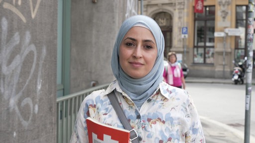 Frau mit Buch in der Hand schaut in die Kamera und lächelt