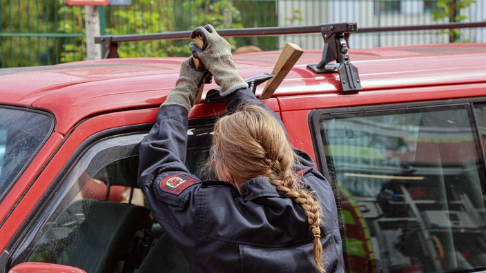 Eine Feuerwehrfrau hebelt an einem Autofenster herum, um dieses zu öffnen.