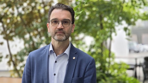 Ein Mann in einem blauen Sakko blickt in die Kamera