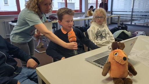 Kinder sitzen vor einem Laptop und werden interviewt.