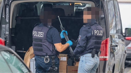 zwei Polizisten holen ein Gewehr aus dem Kofferraum