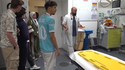 Jugendliche stehen mit einem Arzt in einem Raum voller Schläuche und Kabel