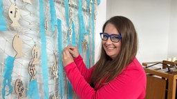 Frau mit Brille steht lachend an einem Fischernetz