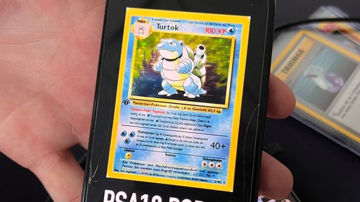 Auf einem Handydisplay wird die Pokemon-Karte "Turtok" angezeigt