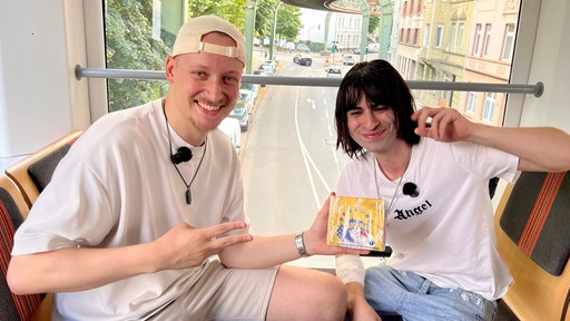 Sam Breckwoldt und Deniz Bal mit einer Box Pokemonkarten in der Schwebebahn