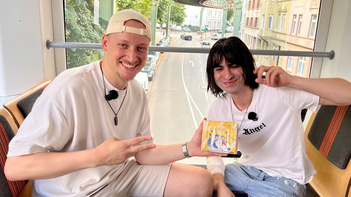 Sam Breckwoldt und Deniz Bal mit einer Box Pokemonkarten in der Schwebebahn