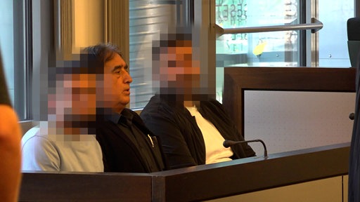 Zwei angeklagte sitzen im Gericht. Ihre Gesichter sind gepixelt.