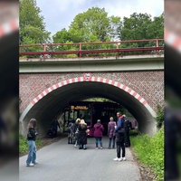 Mehrere Personen stehen vor einer Bahnunterführung, unter der ein Bus stecken geblieben ist.