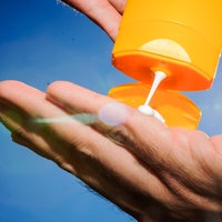 Sonnenmilch aus einer Tube auf eine Hand, im Hintergrund scheint die Sonne von rechts.