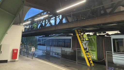Arbeiter steigen auf Gerüst über der Schwebebahn