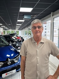 Ein Mann mit grau-meliertem Haar steht in einem Autohaus vor mehreren Neuwagen