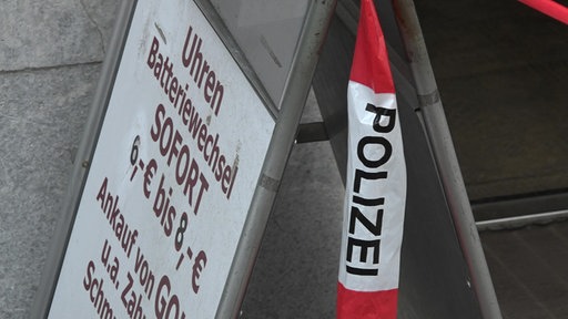 Ein Aufsteller steht vor einem Juwelier, daran hängt ein Flatterband-Stück mit der Aufschrift "Polizei"