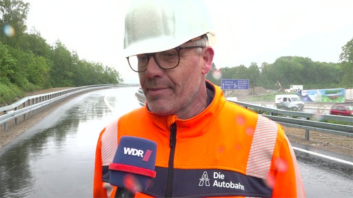 Mann in Warnweste und Schutzhelm guckt in die Kamera