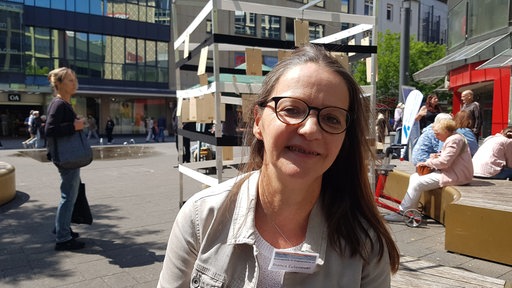 Eine Frau mit Brille und braunen langen Haaren steht in einer Fußgängerzone