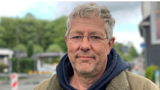 Mann in blauem Kapuzenpullover und mit grauen Haaren schaut in die Kamera