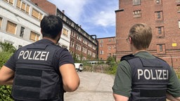 Zwei Polizisten stehen vor der Villa und begutachten diese