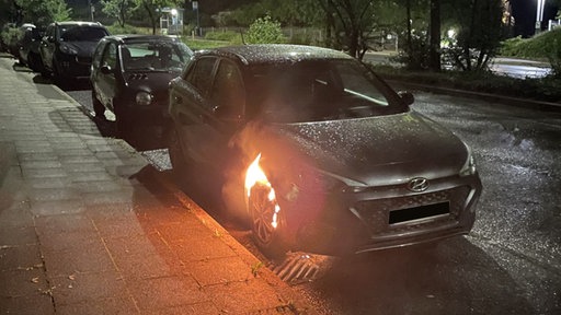 Ein silberner PKW mit brennendem Vorderreifen.
