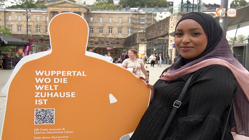 Fahrio Abdirizaak vor einer Pappfigur auf der steht "Wuppertal wo die Welt zuhause ist"