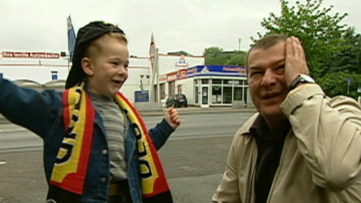 ein Junge mit Deutschland-Schal und ein Mann in brauner Jacke lachen miteinander