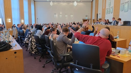 Man sieht den Wuppertaler Stadtratsaal gefüllt mit Menschen. Viele heben die Hand.