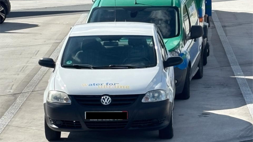 ein weißer und ein grüner PKW  hintereinander auf einer grauen Straße