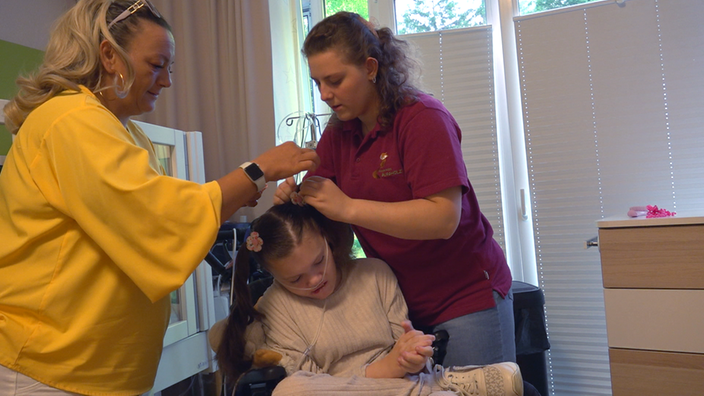 FSJ-lerin macht Patientin im Rollstuhl die Haare, mit dabei ist die Mutter