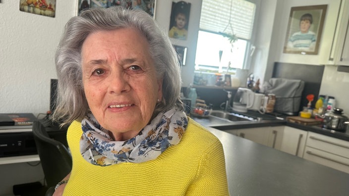 Ältere Frau mit mittellangen grauen Haaren, einem Halstuch und einem gelben Pullover