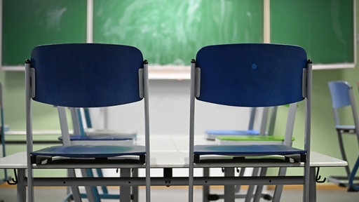 Zzwei auf den Tisch hochgestellte blaue Stühle vor einer grünen Tafel