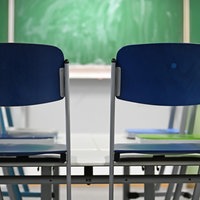 Zzwei auf den Tisch hochgestellte blaue Stühle vor einer grünen Tafel