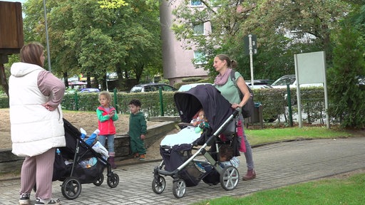 Zwei Mütter mit Kinderwagen treffen sich auf dem Spielplatz