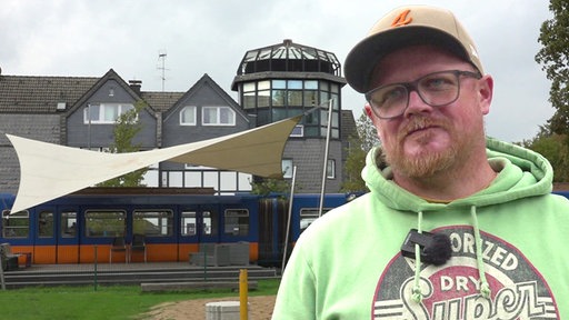 Mann mit Brille und Baseball-Cap steht auf dem Spielplatz