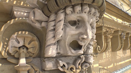 Ein Gesicht aus Stein mit weit aufgerissenen Augen und Mund. Ein Kunstwerk an der Fassade der Stadthalle.