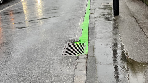 Neongelbes Wasser fließt am Straßenrand entlang in den Gulli