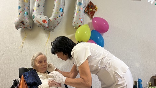 Lieselotte Debry und eine Pflegerin mit Geburtstagsluftballons im Hintergrund.