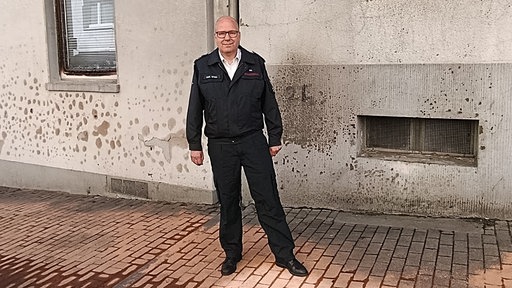 Ein Mann in Uniform steht vor einer Hauswand 