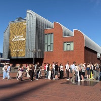 Menschenmasse vor einem Gebäude auf der ein Kusama Plakat hängt