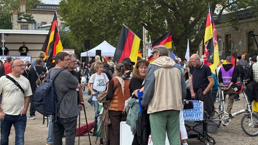 Mehrere Menschen haben sich für eine Demo versammelt, einige halten Deutschlandfahnen hoch.
