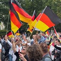 Mehrere Menschen haben sich für eine Demo versammelt, einige halten Deutschlandfahnen hoch.