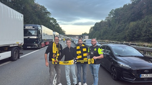 Fußballfans stehen auf einer Autobahn und lächeln