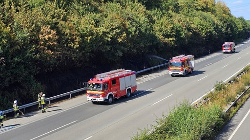 Einsatzfahrzeuge der Feuerwehr stehen auf der A2 bei Bielefeld und versuchen, den Böschungsbrand zu löschen