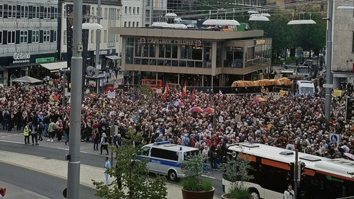 Hunderte Menschen stehen auf einem Platz, viele halten Fahnen hoch.