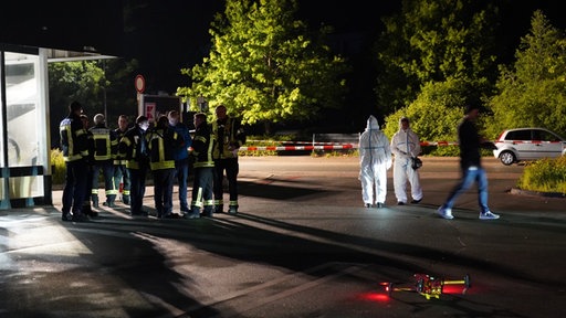 Eine Gruppe Feuerwehrleute und Ermittler sowie eine Drohe im Einsatz am Tatort