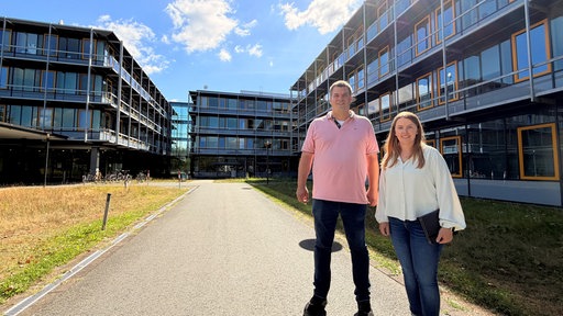 Zwei glückliche Menschen stehen vor den Gebäuden der Stadtverwaltung Paderborn.