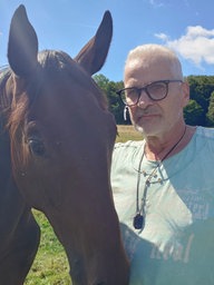 Tierarzt Torsten Köhler steht auf einer Koppel mit seinen gesunden Pferden.