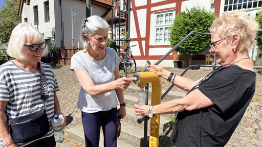 Drei Personen füllen eine Flasche am Trinkbrunnen in Werther. 