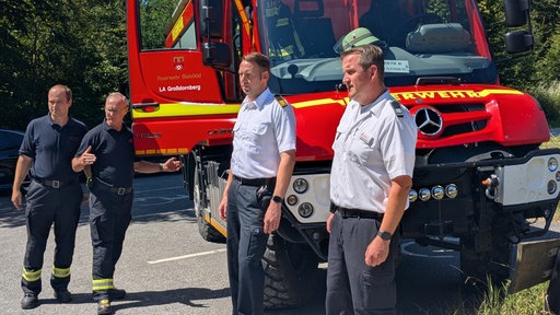 Vier Bielefelder Feuerwehrmänner stehen vor einem geländegängigen Tanklöschwagen.