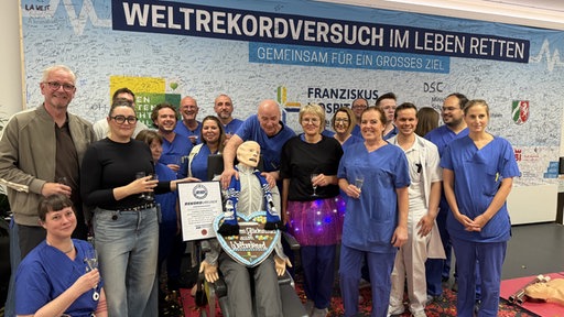 Eine Gruppe mit Sektgläsern neben einer Puppe