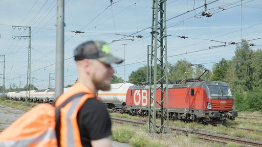 Lokführer René Breuer steht am Gleis, im Hintergrund sieht man einen Zug